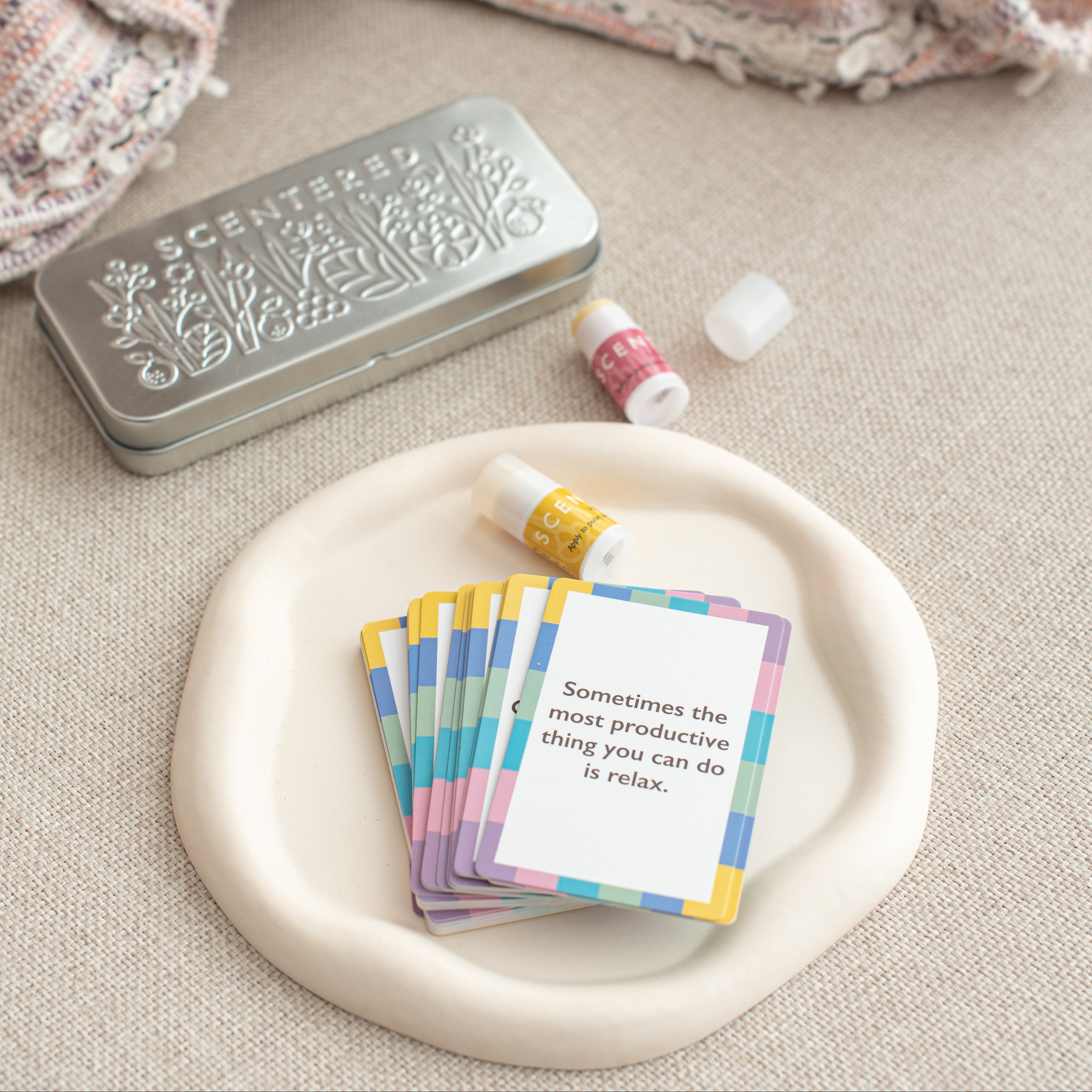 A tin box, a pack of cards, and two mini balms are resting on the sofa.